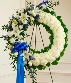 Corona funeral de crisantemos, rosas y liliums blancos con cinta azul